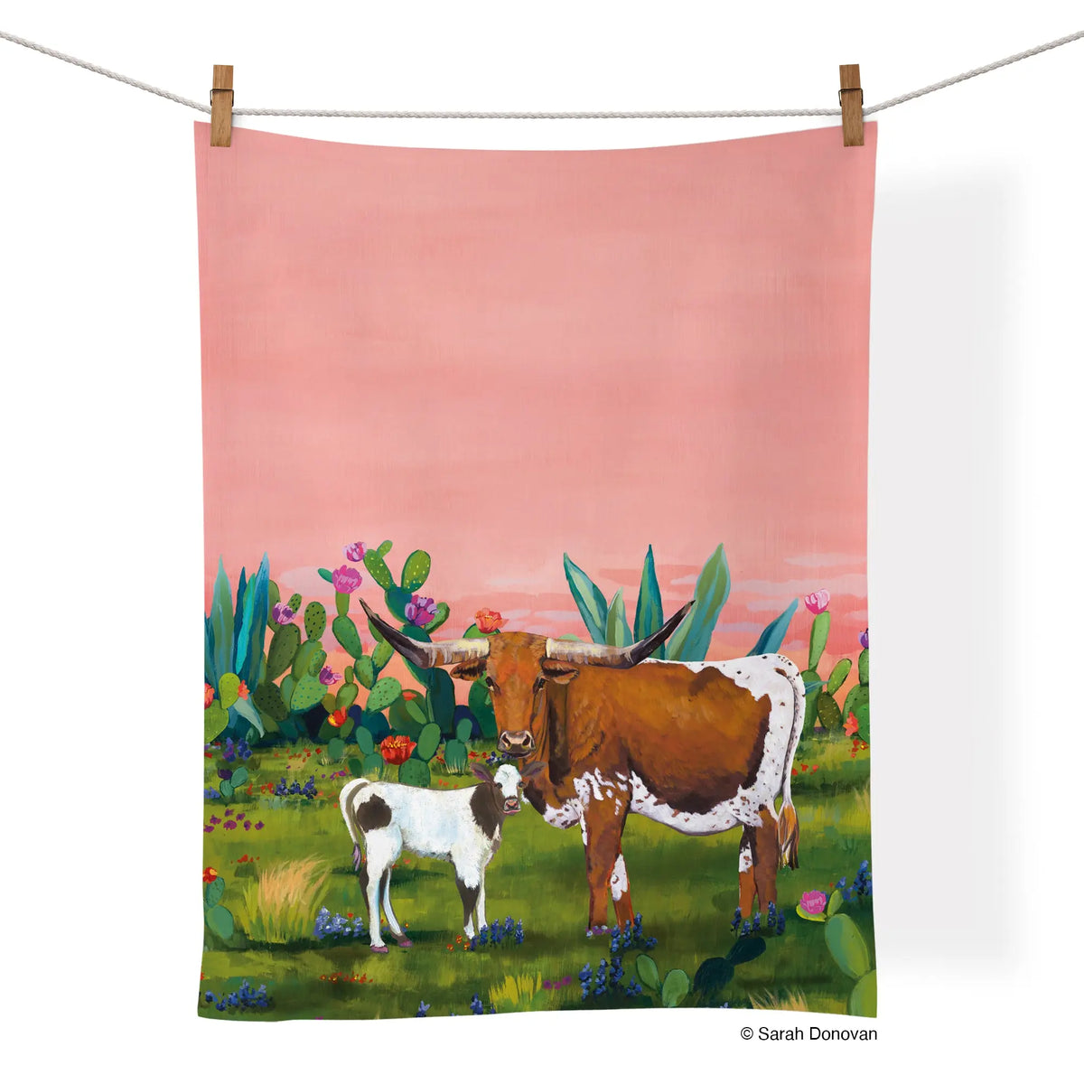 Cotton tea towel featuring a longhorn and calf in a desert landscape with cacti against a pink sunset background.