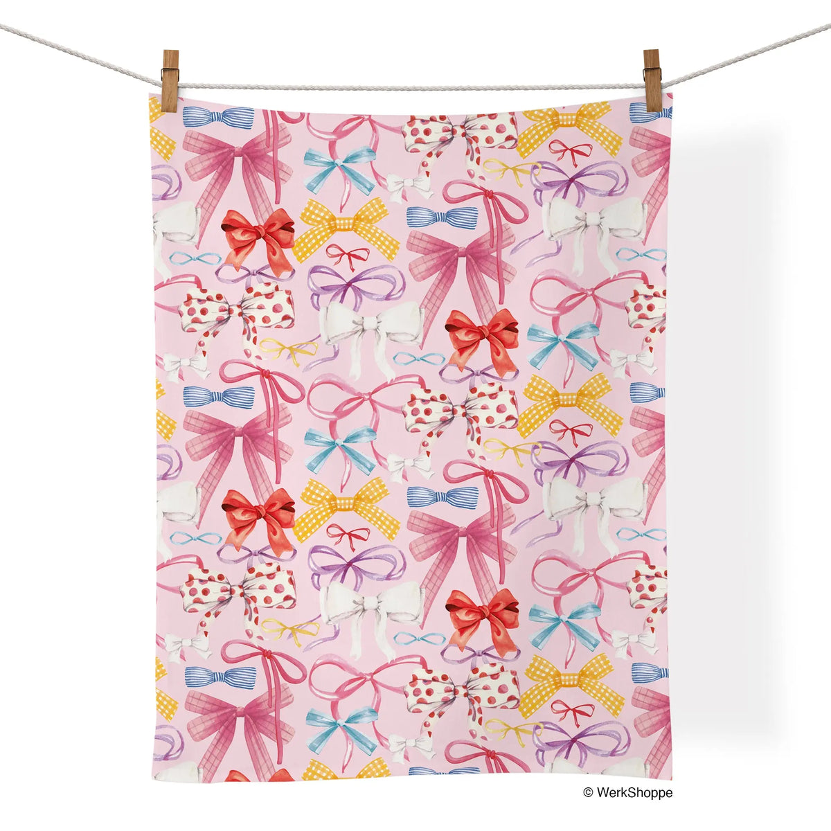 Cotton tea towel with a repeating pattern of watercolor bows in pink, yellow, blue, red, and white on a pink background.