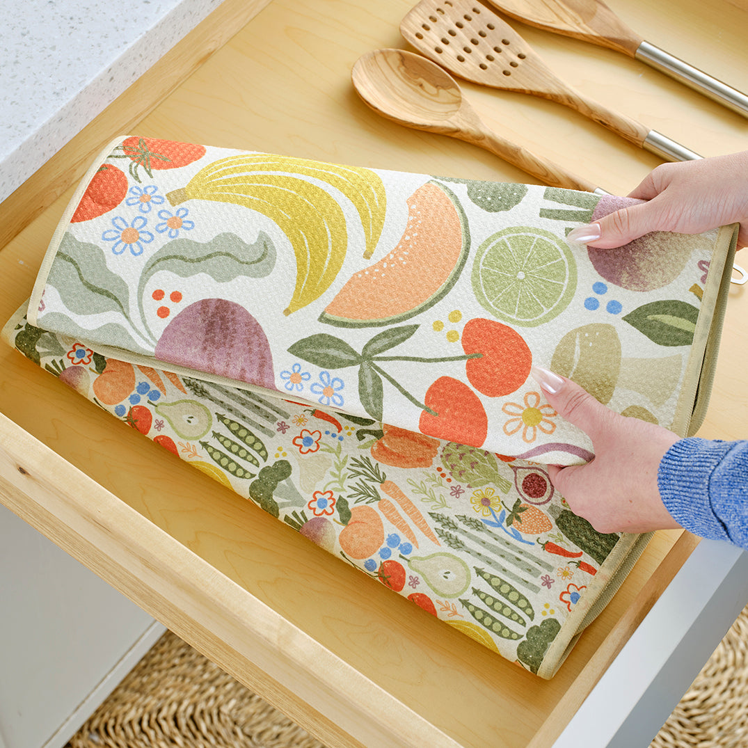 Soft, fabric dish drying mat featuring a colorful, patterned print of fruits, vegetables, and small blue flowers.