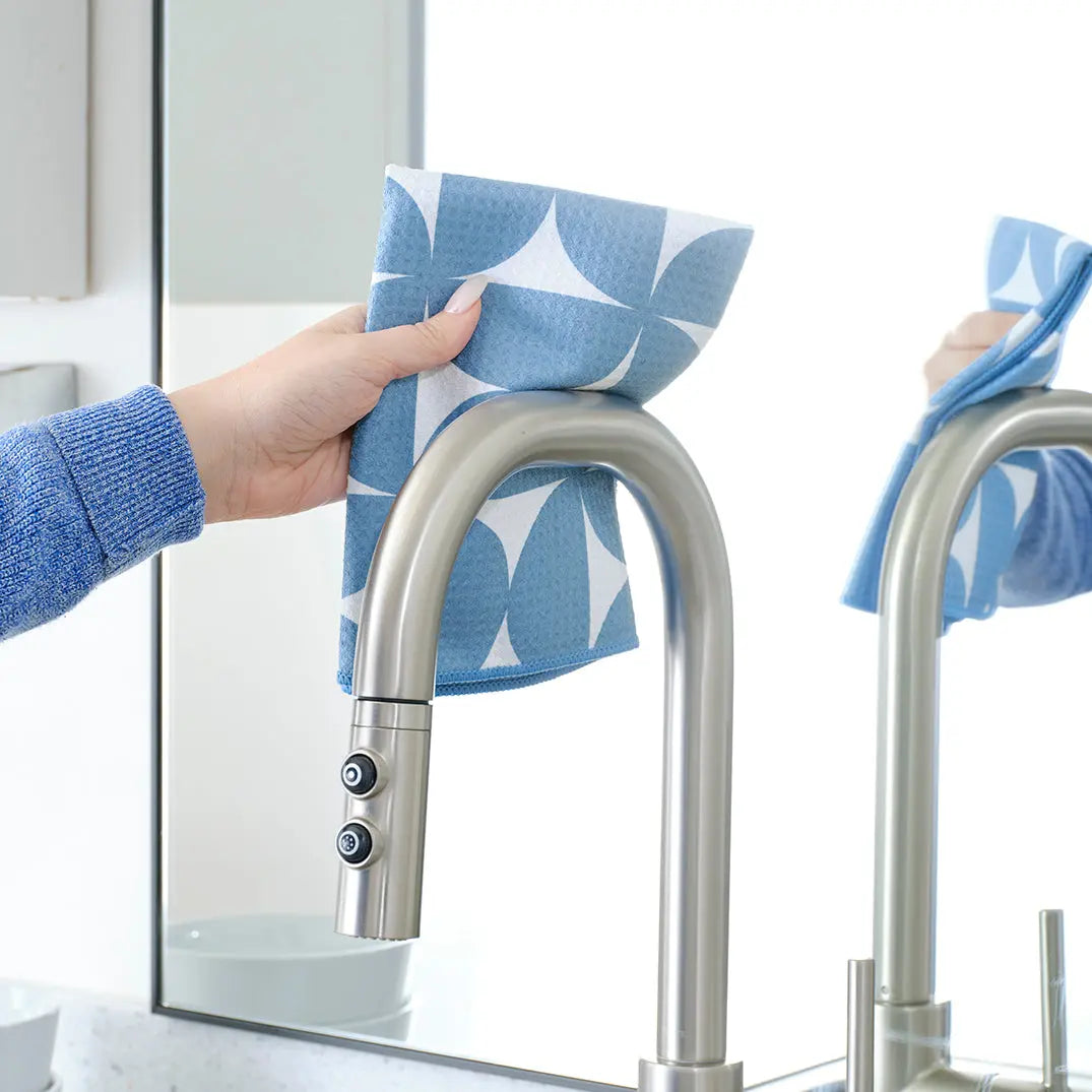 Hand cleaning a chrome faucet with a blue and white patterned absorbent cleaning cloth.