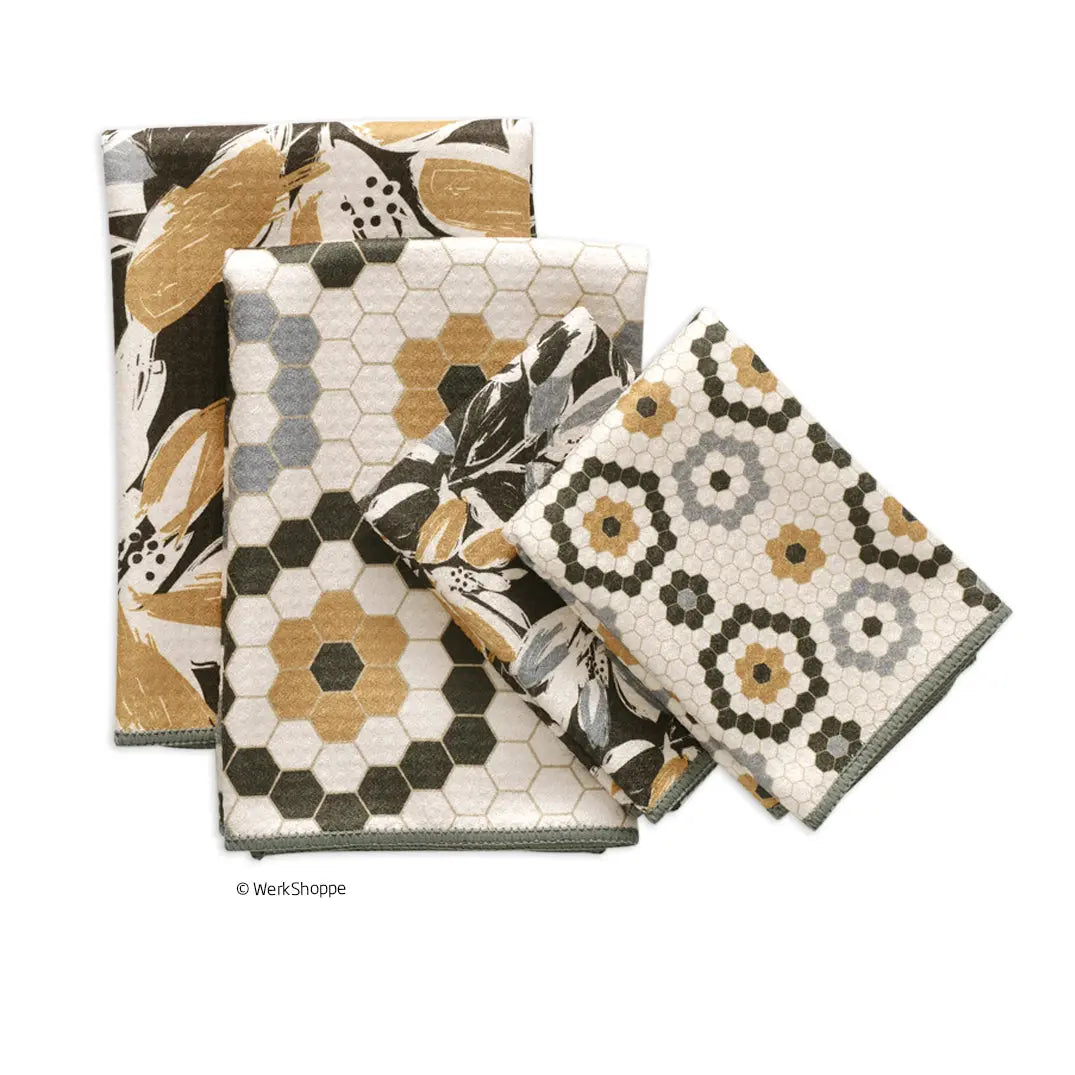 Three folded towels featuring black, gold, and grey geometric honeycomb patterns and abstract organic leaf motifs.