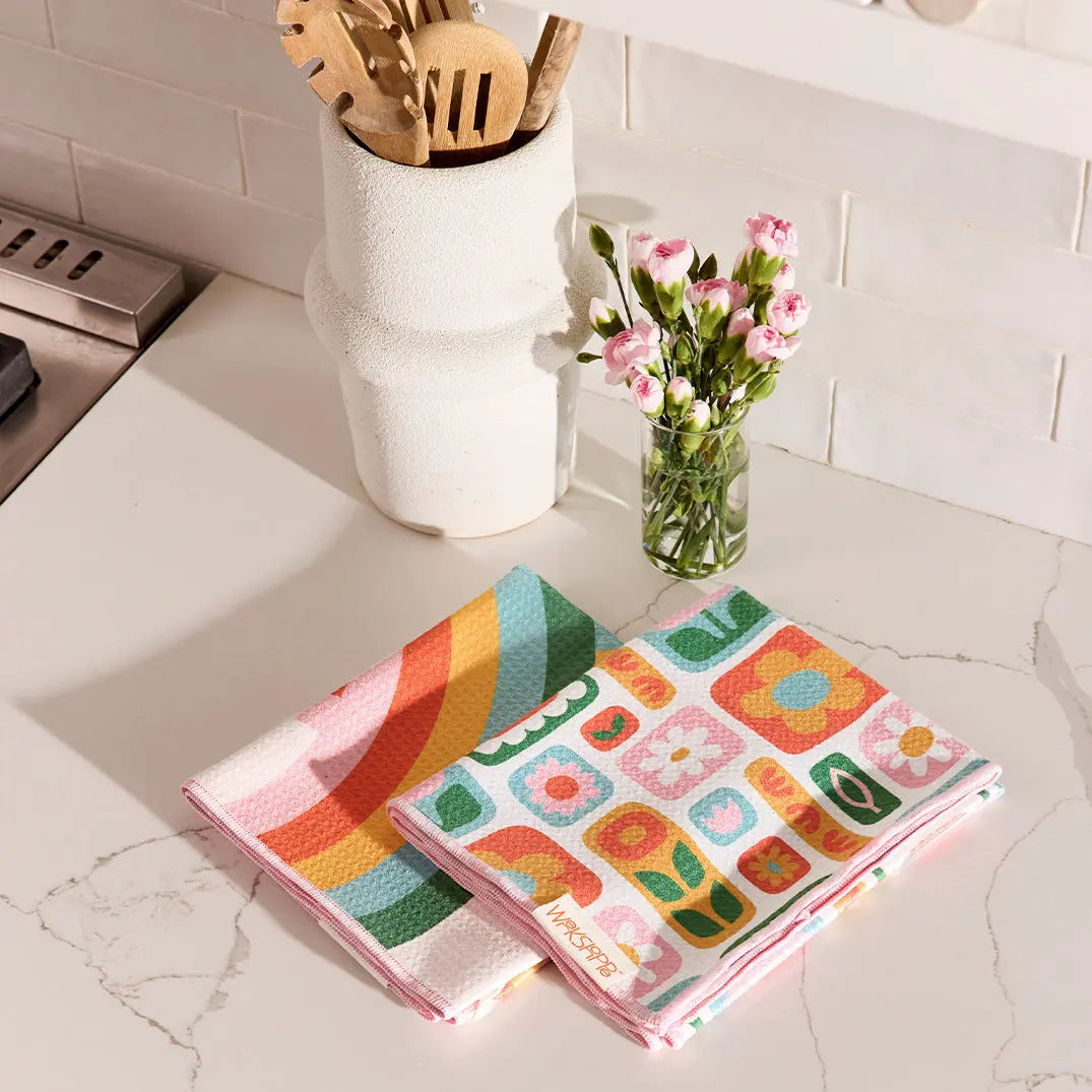Two microfiber towels featuring retro daisy and rainbow patterns in vibrant colors, folded on a marble countertop.