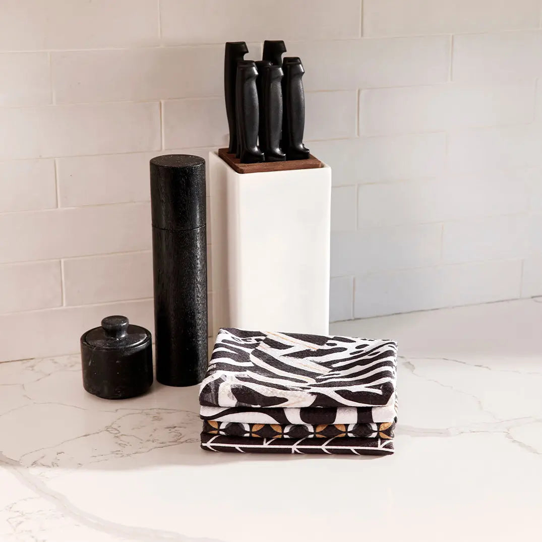 A stack of folded microfiber towels featuring a black and white mod floral tile pattern on a marble countertop.