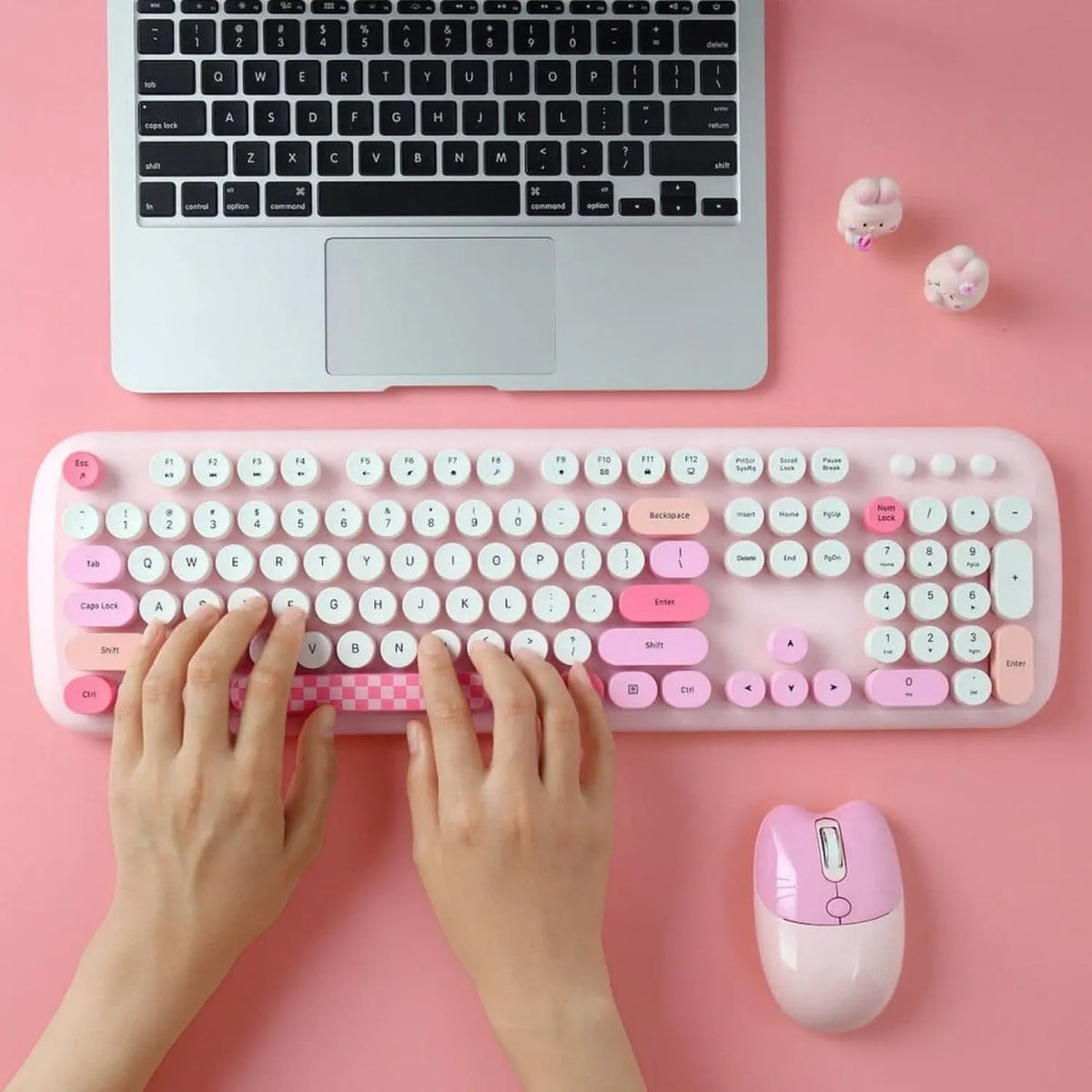 Pink wireless keyboard and mouse set with round keys, check pattern spacebar, and ergonomic design on a pink desk.