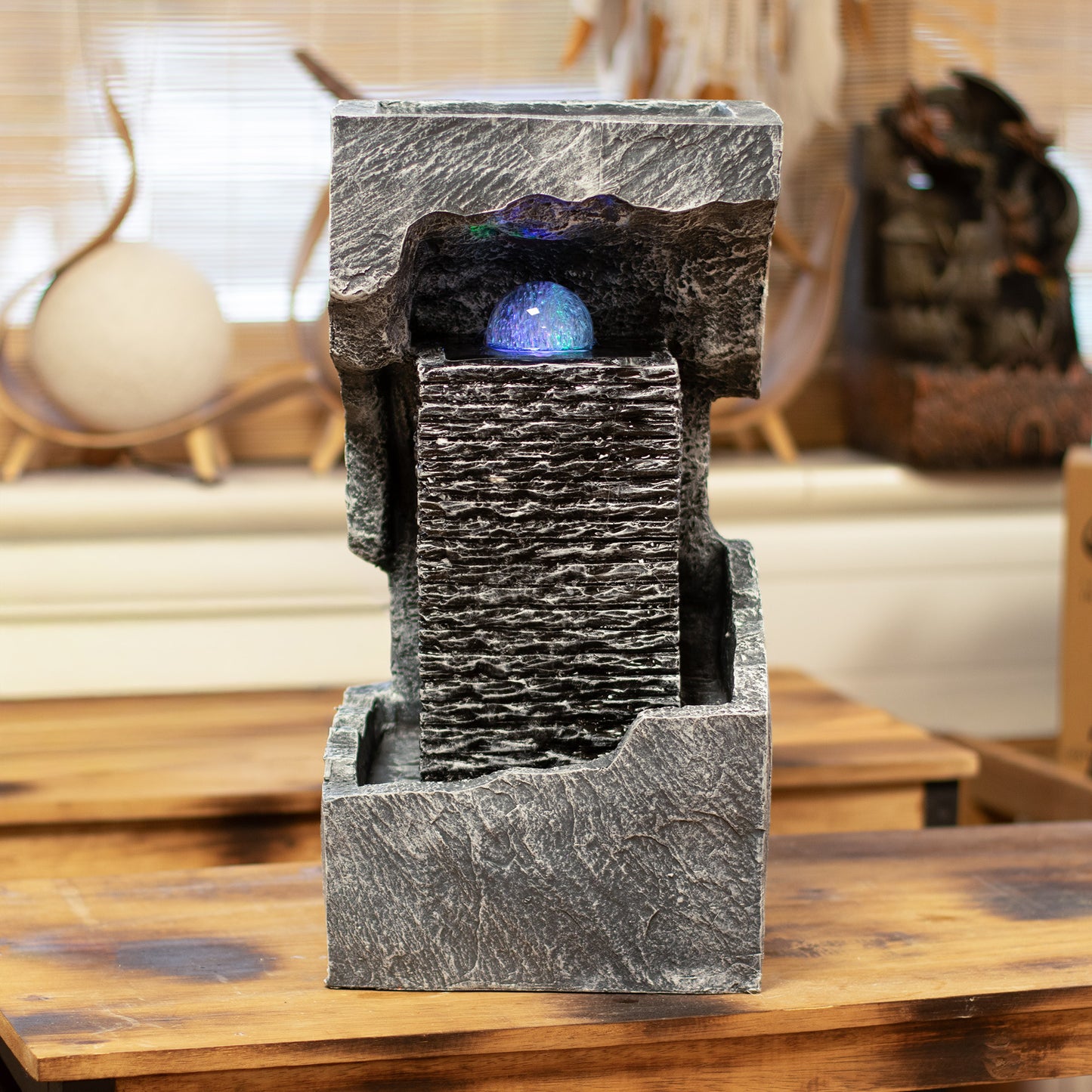 Fuente decorativa de resina gris con esfera iluminada, estilo moderno y acabado textura de roca.
