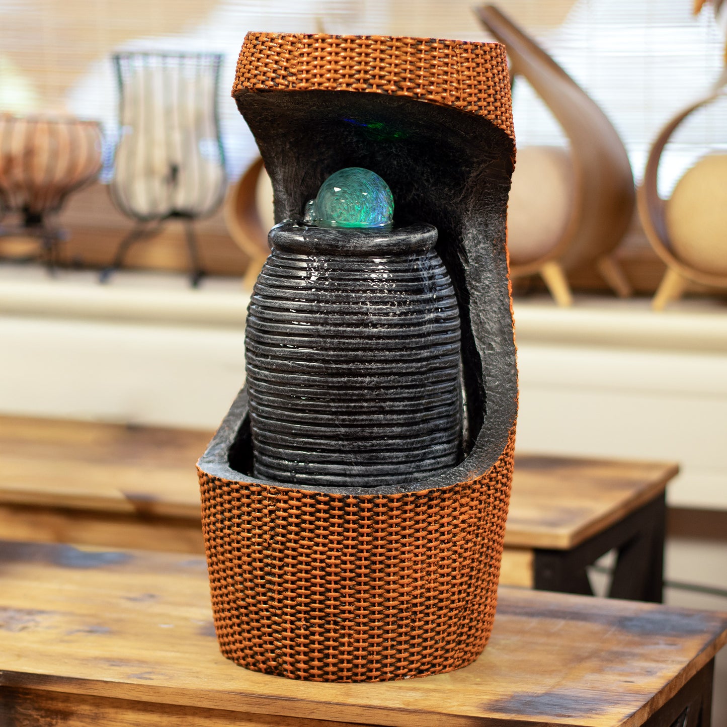 Fuente decorativa de cerámica negra con detalles en mimbre naranja y esfera iridiscente, ideal para interiores.