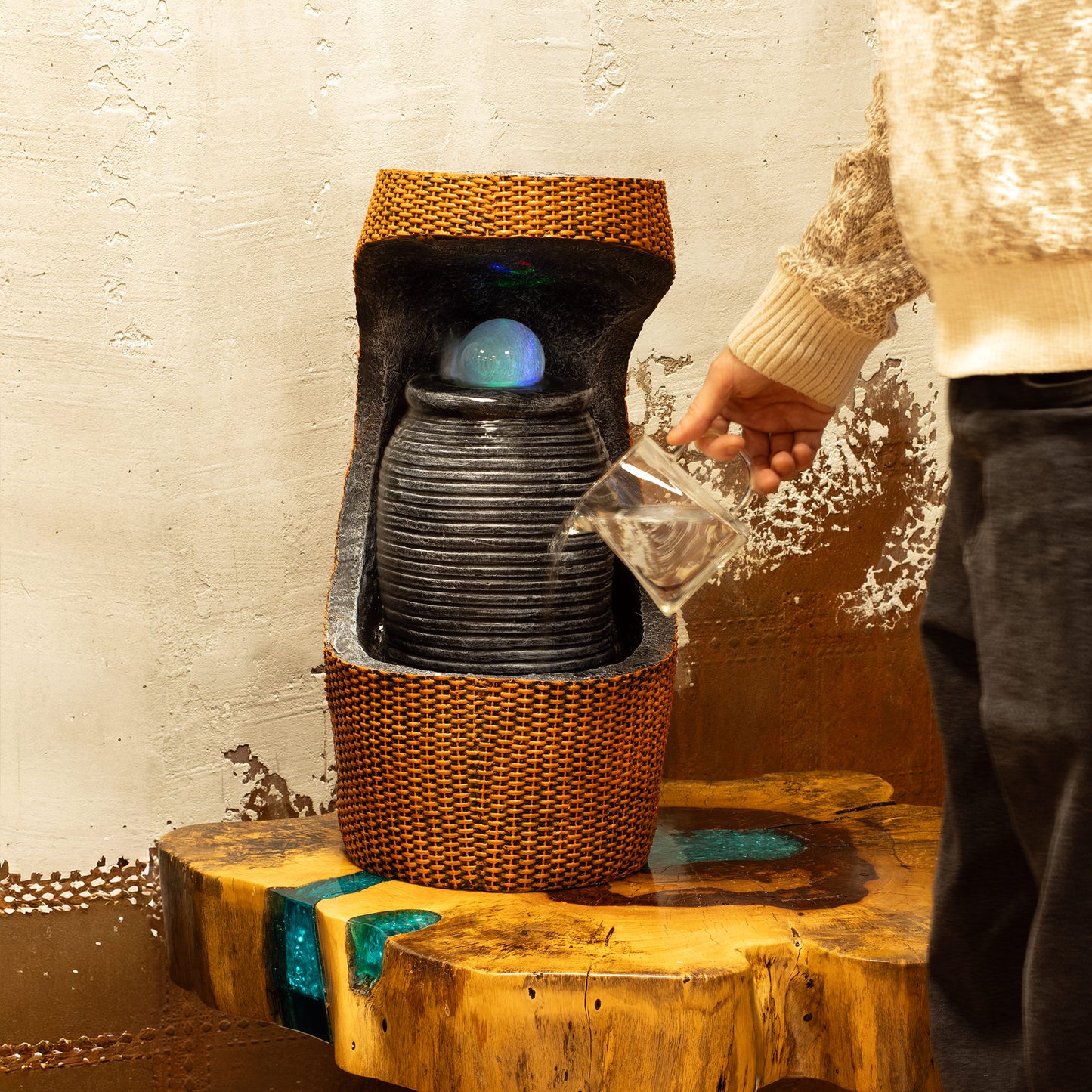 Fuente decorativa de cerámica negra con detalles en mimbre, luz LED y agua que fluye, ideal para interiores.