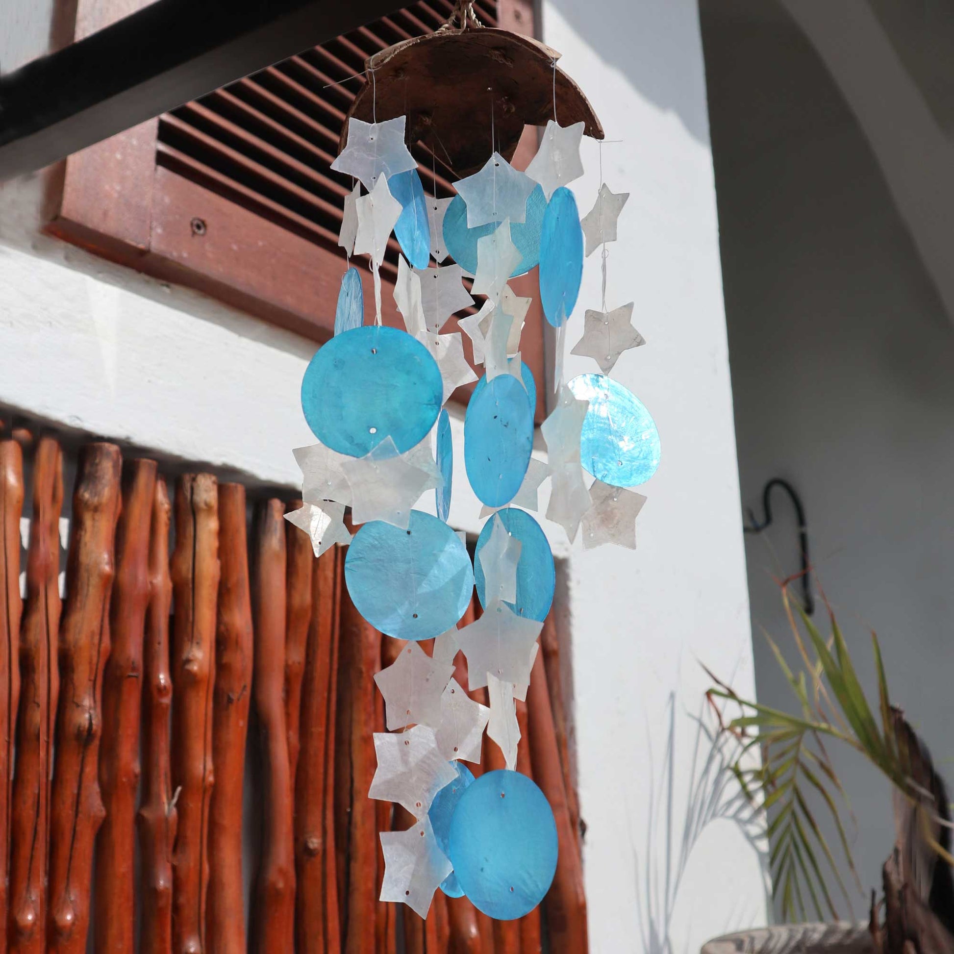Carillón de 30 cm con base de coco y piezas de capiz en forma de estrellas y círculos blancos y azules.