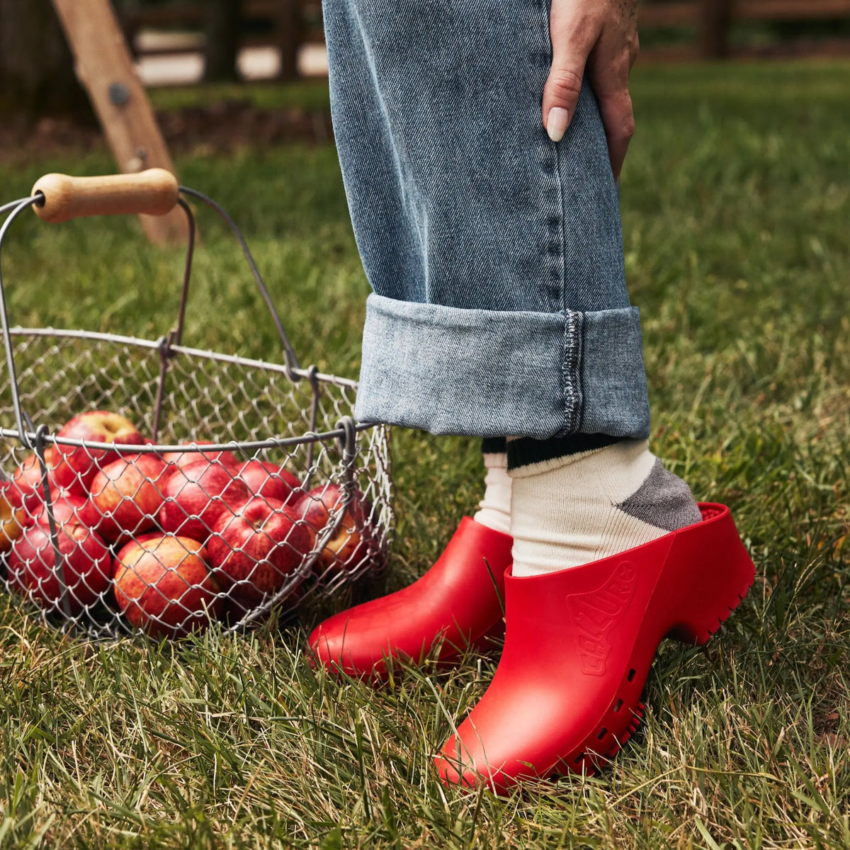 Bright red clogs made of durable material, paired with rolled-up denim and cozy socks, perfect for outdoor activities.