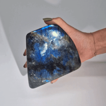 Piedra labradorita azul brillante en mano; forma irregular con destellos metálicos y textura natural.