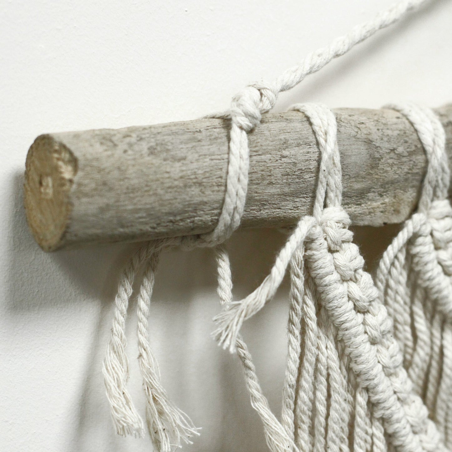 Macramé decorativo en color crema con barra de madera, ideal para interiores boho y naturales.