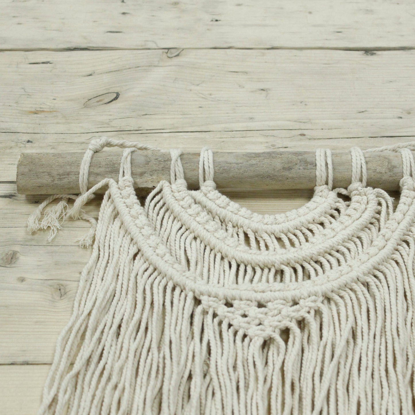 Tapiz de macramé beige con detalles en madera, estilo bohemio, perfecto para decoración de pared.