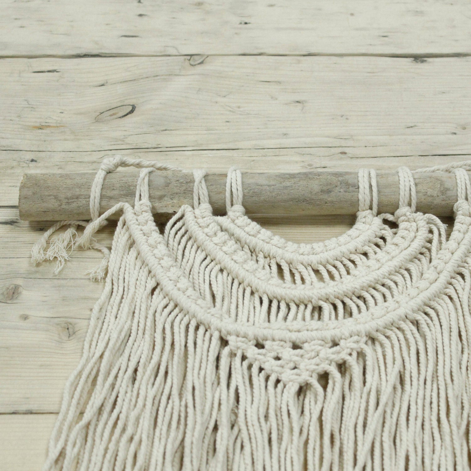 Tapiz de macramé beige con detalles en madera, estilo bohemio, perfecto para decoración de pared.