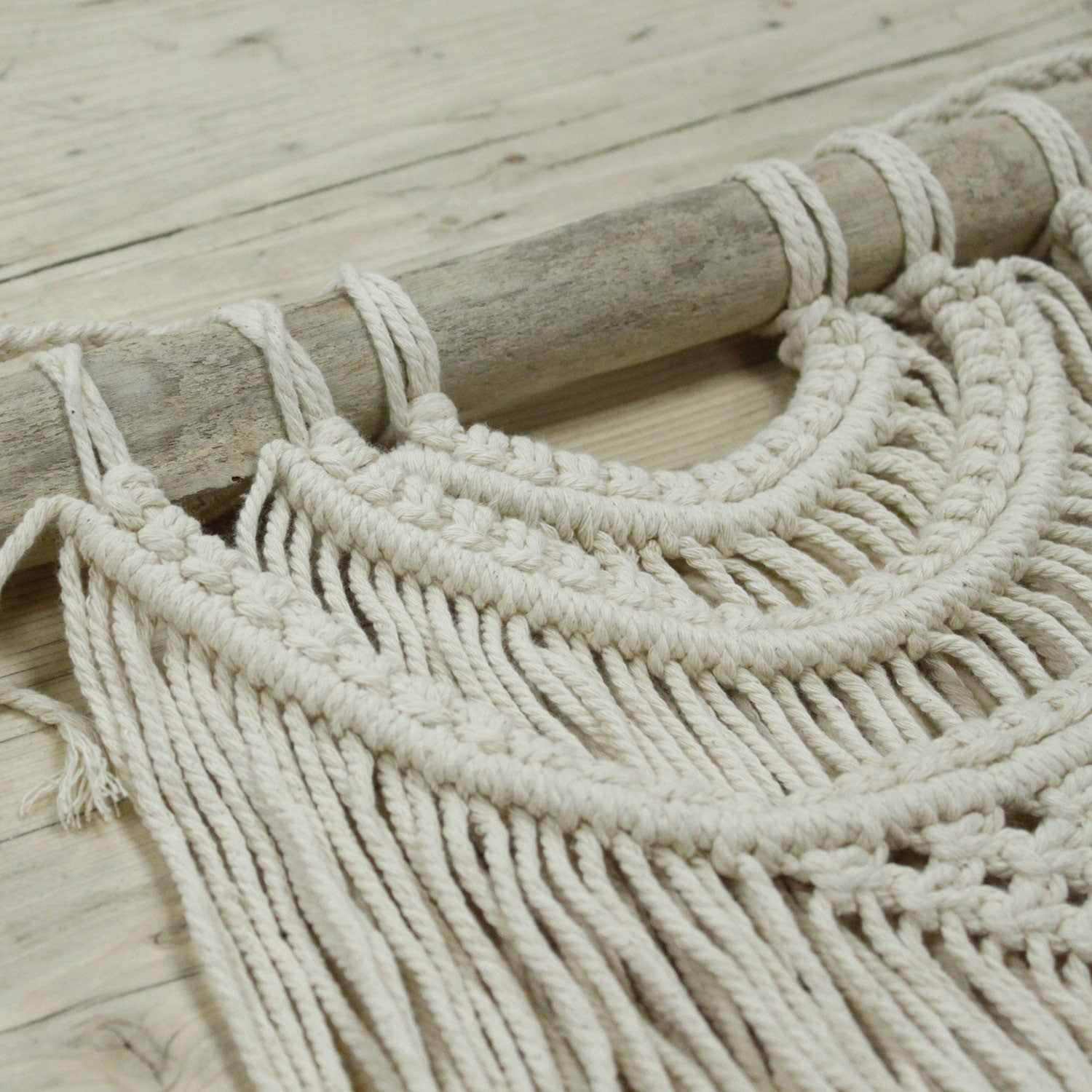 Tapestry de macramé beige, hecho a mano con cuerdas de algodón, estilo bohemio, colgado en una barra de madera.