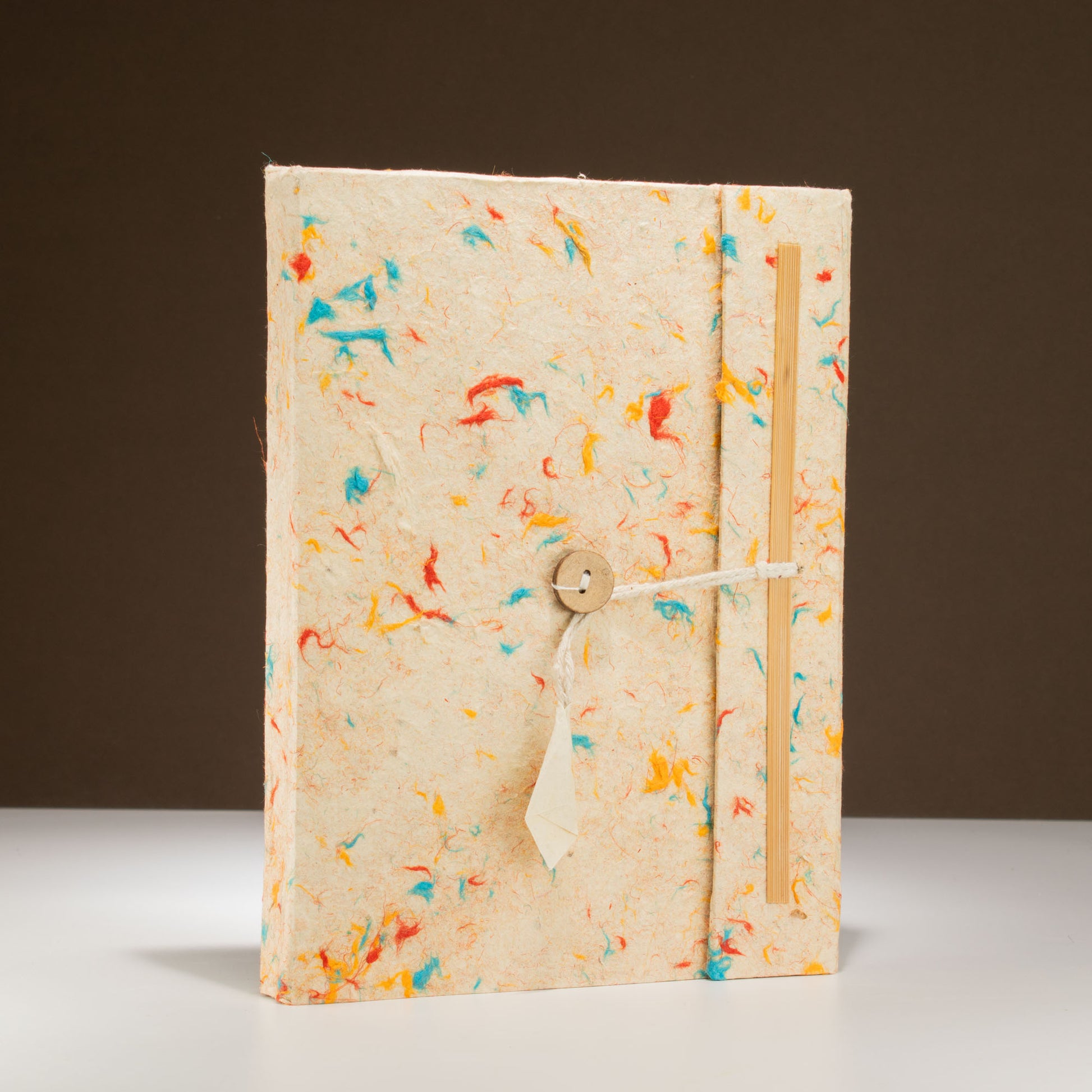Handcrafted cream paper notebook with colorful flecks, wooden closure, and twine tie, perfect for journaling.