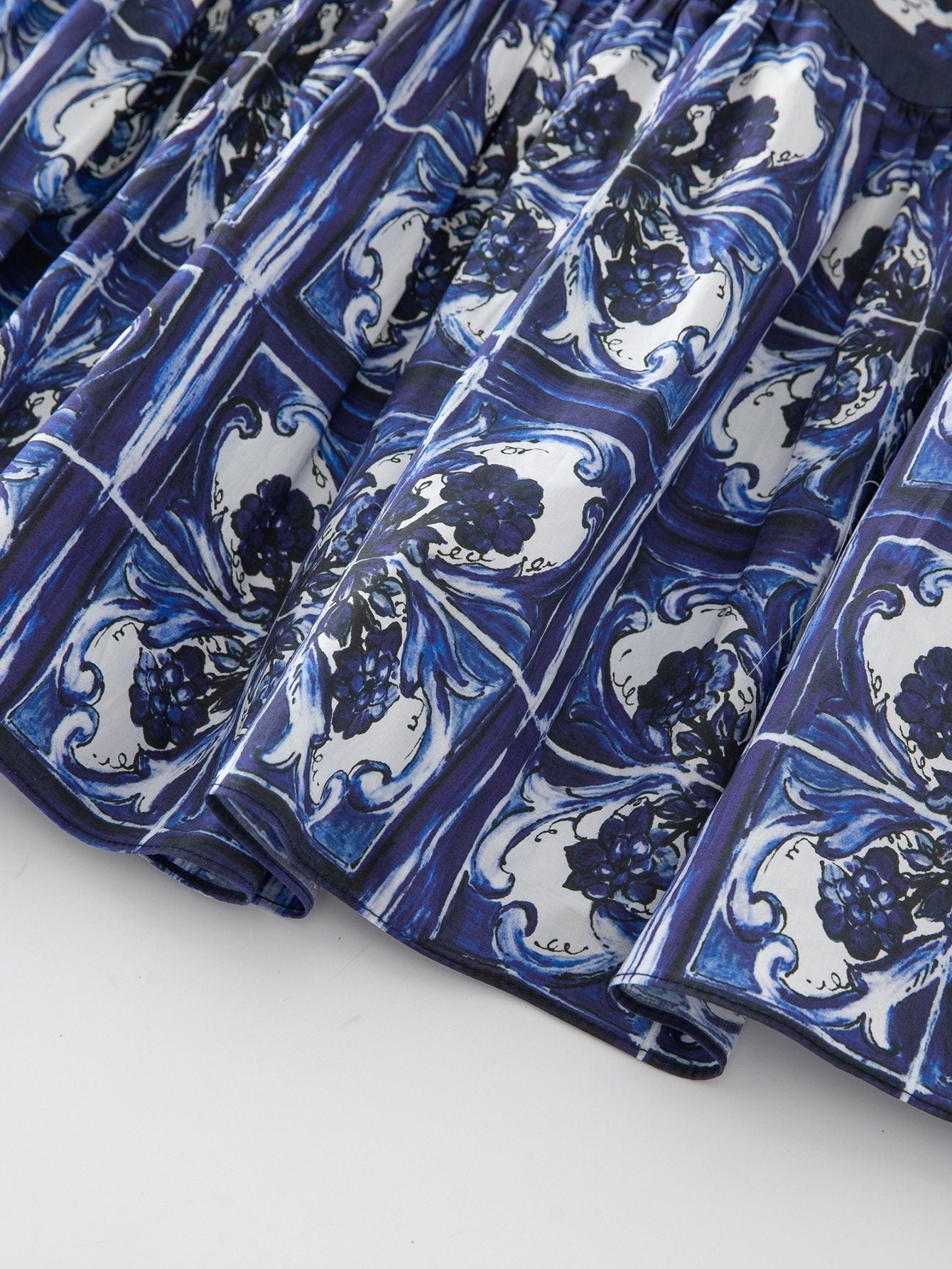 Blue floral print pleated skirt, featuring intricate white and navy tile patterns, made from lightweight fabric.