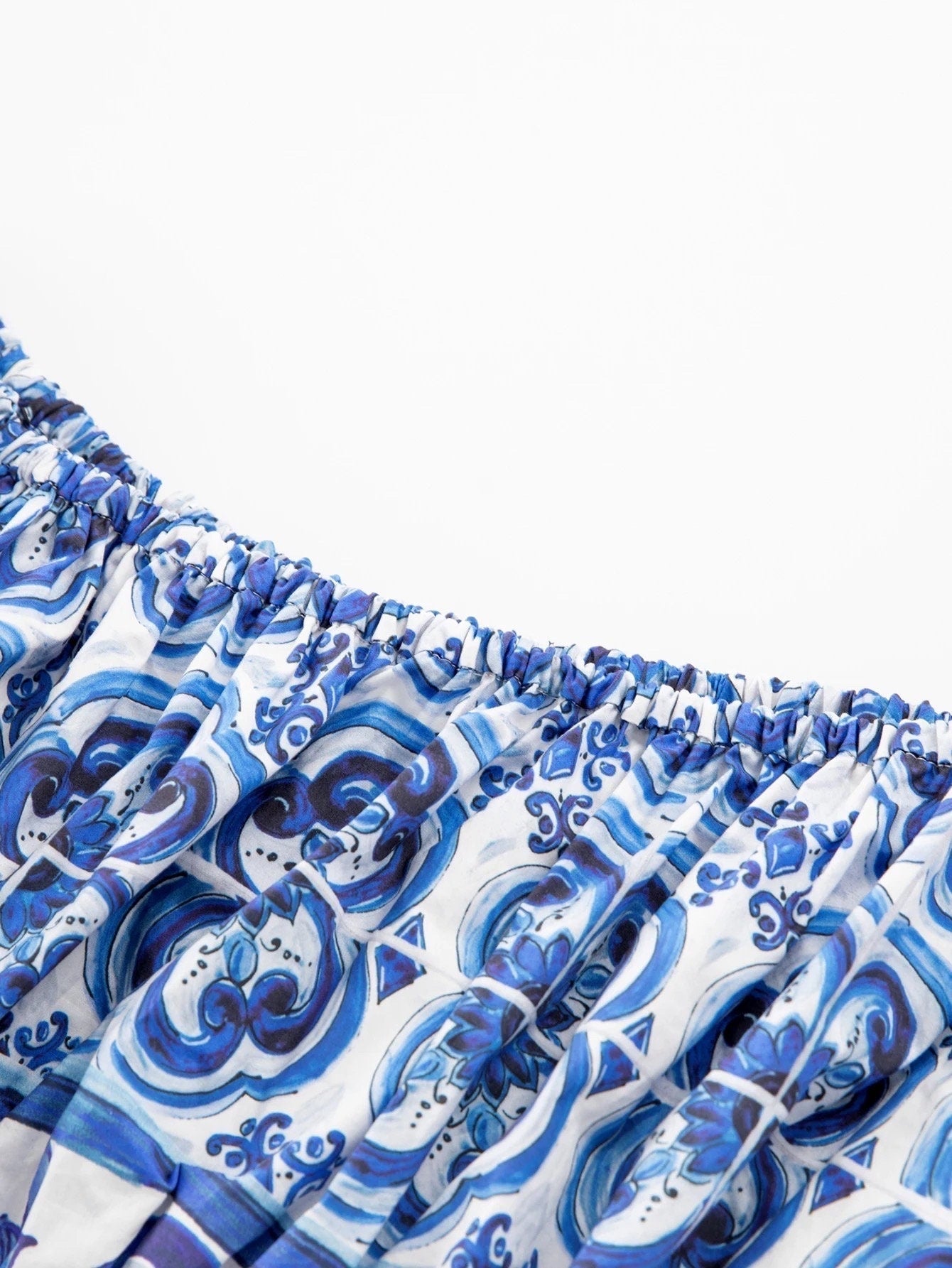 Blue and white patterned off-shoulder dress with elastic neckline, featuring intricate swirl designs in lightweight fabric.
