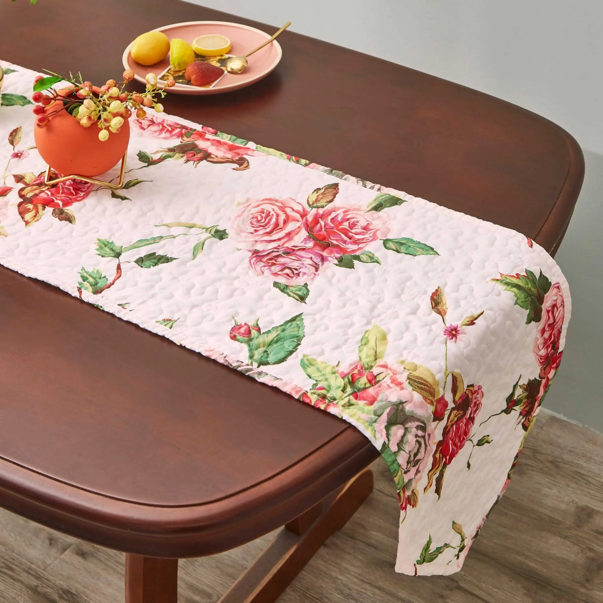 Quilted pink dining table runner featuring a romantic white and pink rose floral pattern on a dark wood table.