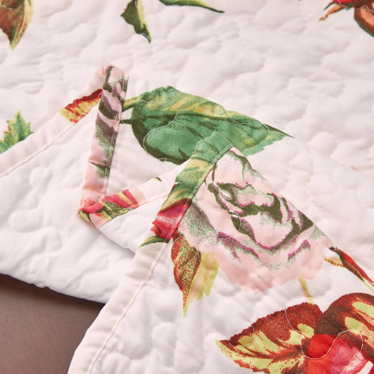 Quilted white dining table runner featuring a romantic pink rose and green leaf floral pattern with scalloped edges.