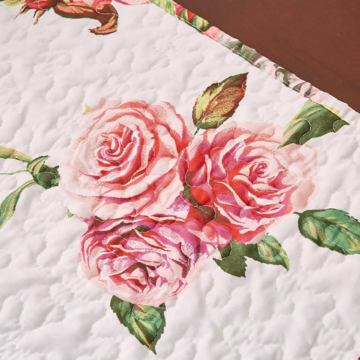 White quilted table runner featuring romantic pink rose patterns and green leaves on a textured, stitched fabric.