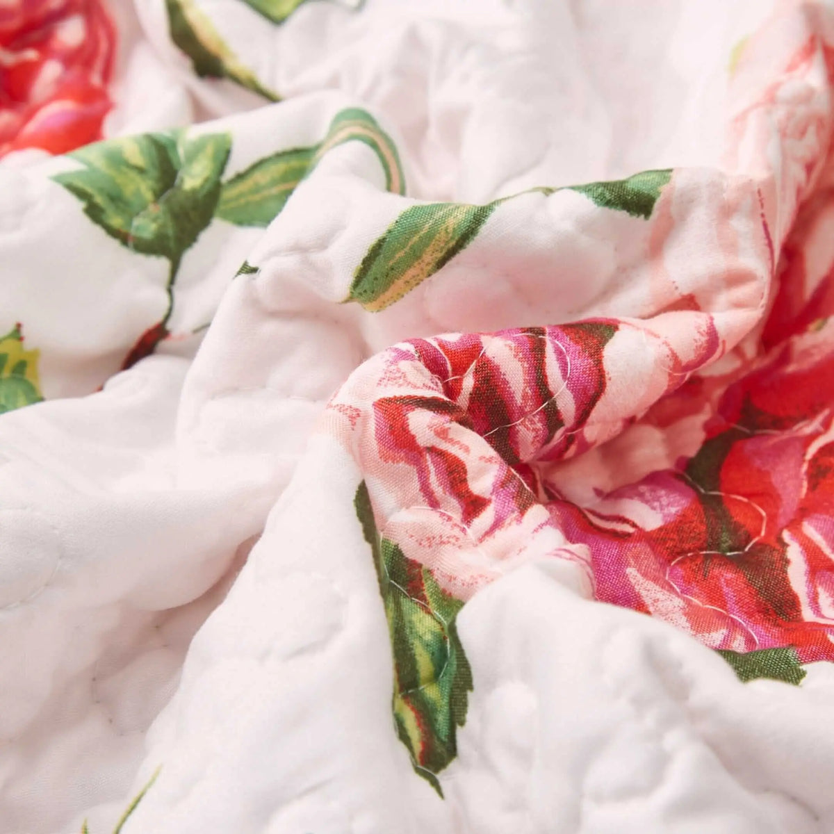 Close-up of a quilted fabric table runner with pink rose floral patterns and green leaves on a white background.