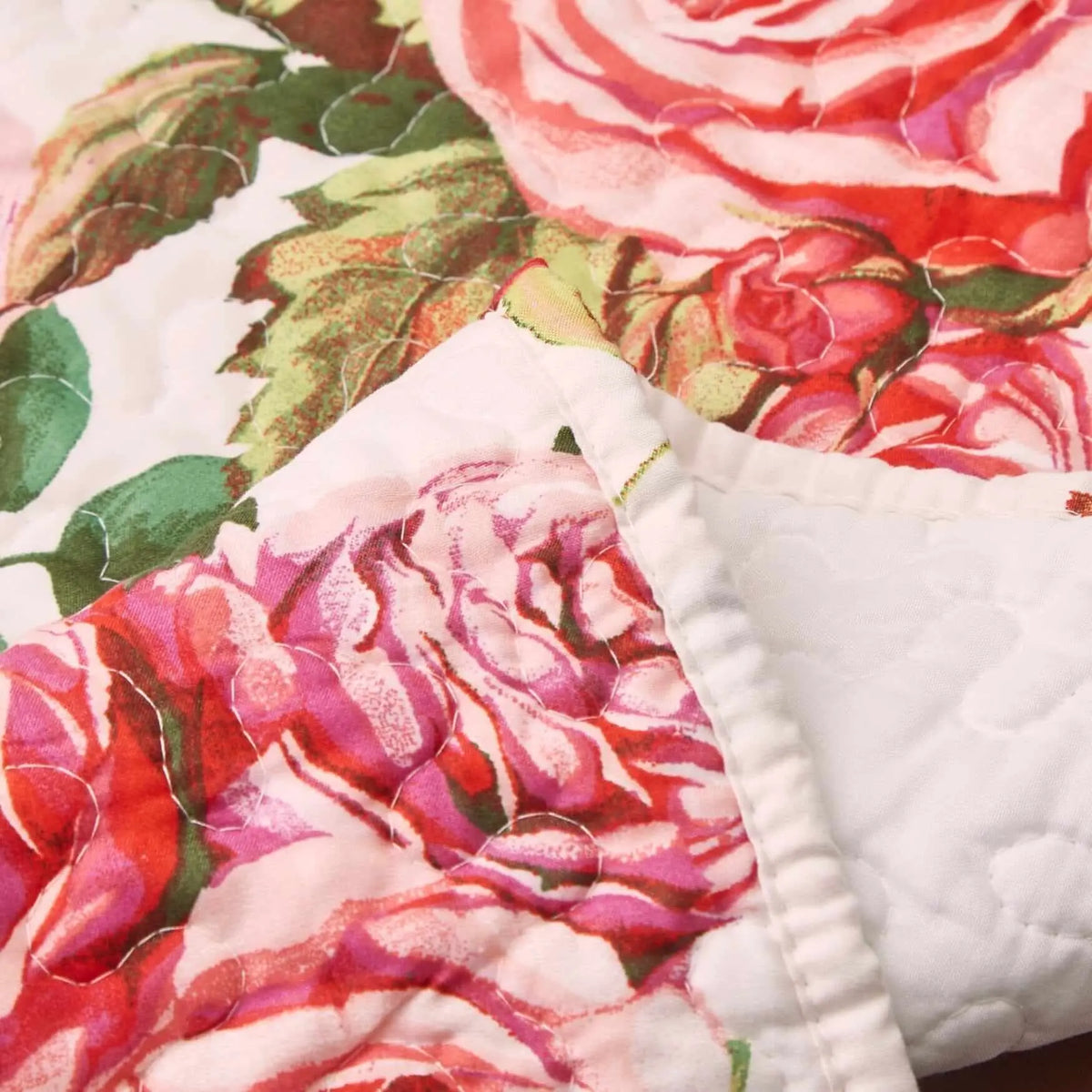 Quilted table runner with pink and red rose floral pattern on white fabric, featuring stitched scalloped detailing.