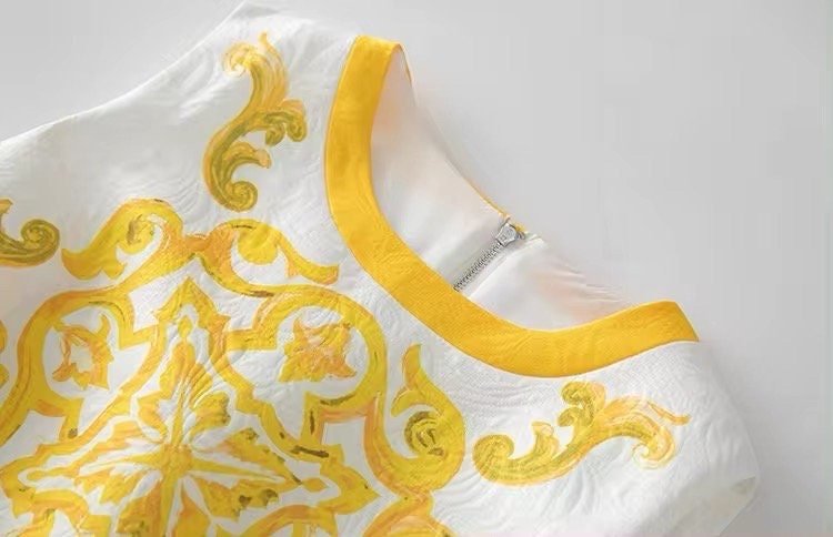 White dress with bold yellow baroque print and round neckline, featuring a stylish zipper closure at the back.