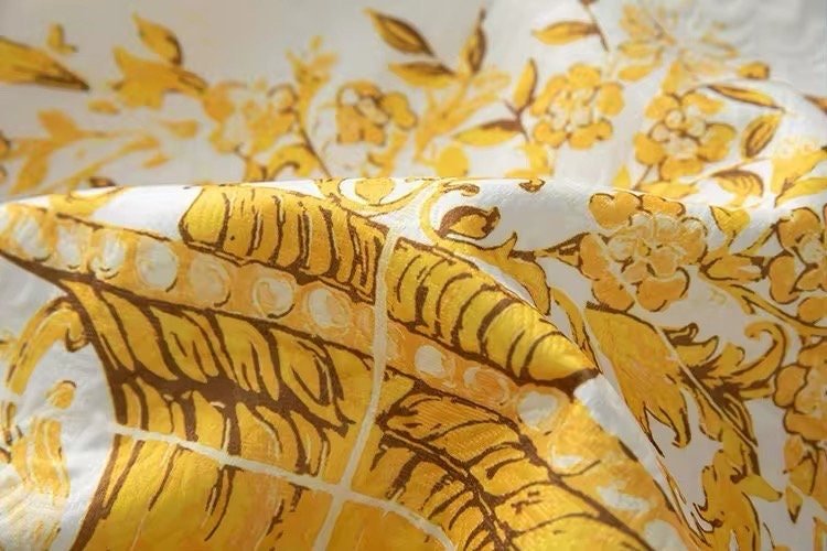 Yellow floral print fabric with intricate leaf designs on a white background, perfect for summer apparel or home decor.