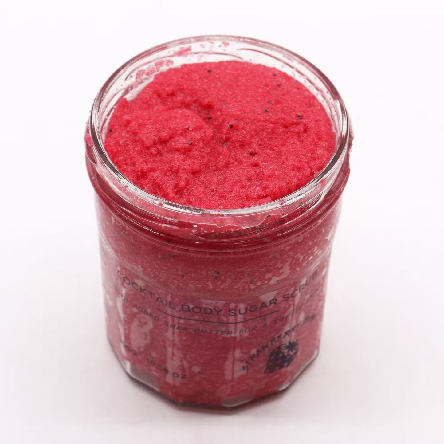 Tarro de vidrio con exfoliante corporal de azúcar rojo brillante con semillas, de textura granulada y aroma a fresa.