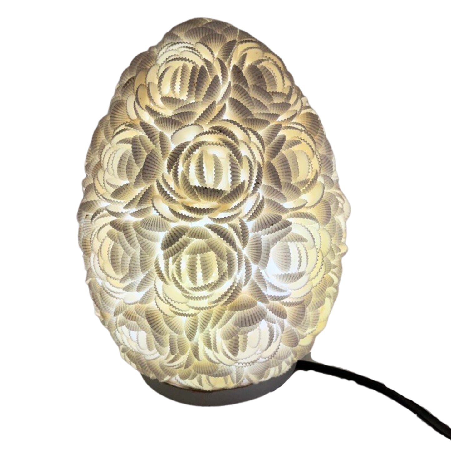 Lámpara boho ovalada de 20cm, hecha con pequeñas conchas blancas dispuestas en forma de rosas, emitiendo luz cálida.