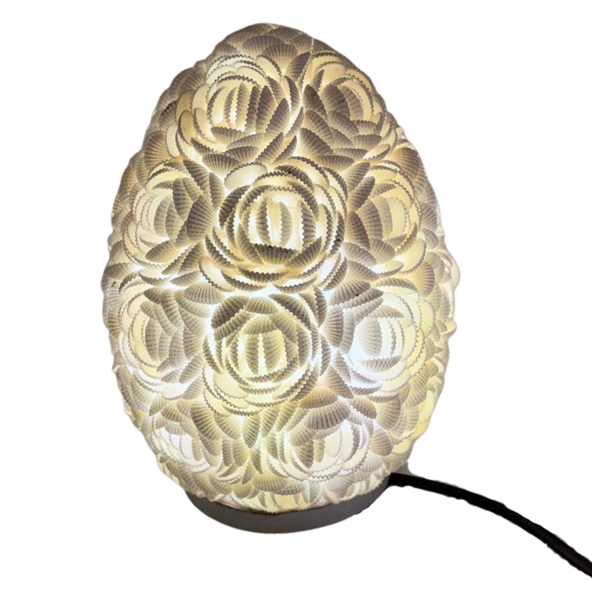 Lámpara boho ovalada de 20cm, hecha con pequeñas conchas blancas dispuestas en forma de rosas, emitiendo luz cálida.