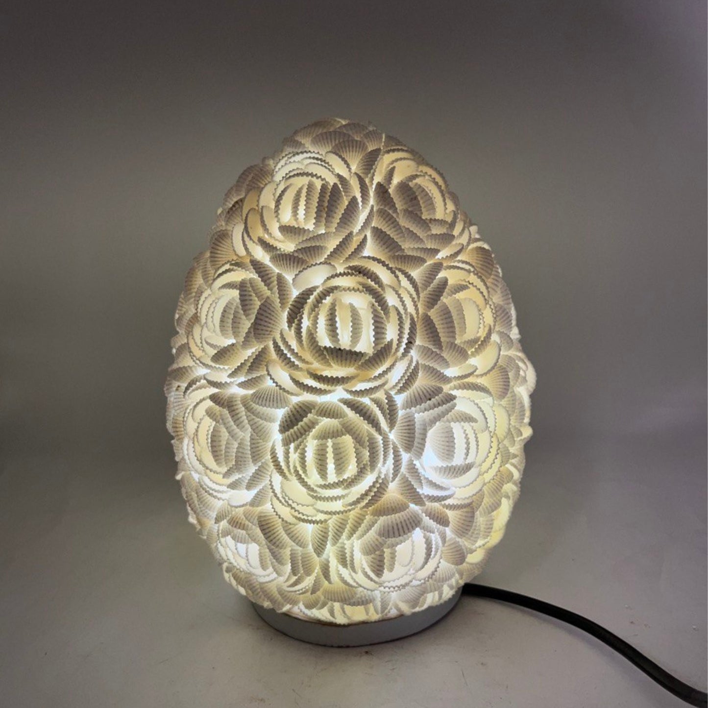 Lámpara boho ovalada de 20cm, hecha con conchas marinas blancas dispuestas en forma de rosas, con luz cálida interna.