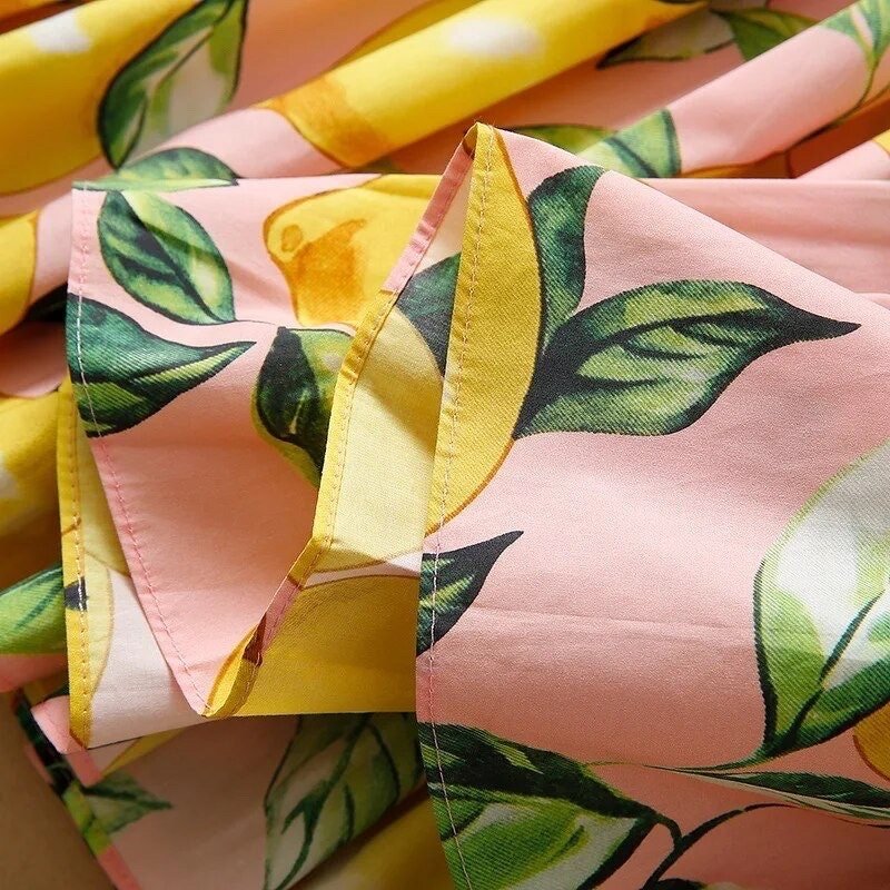 Pink lemon-patterned fabric with vibrant yellow and green leaves, featuring a smooth and soft textile finish.