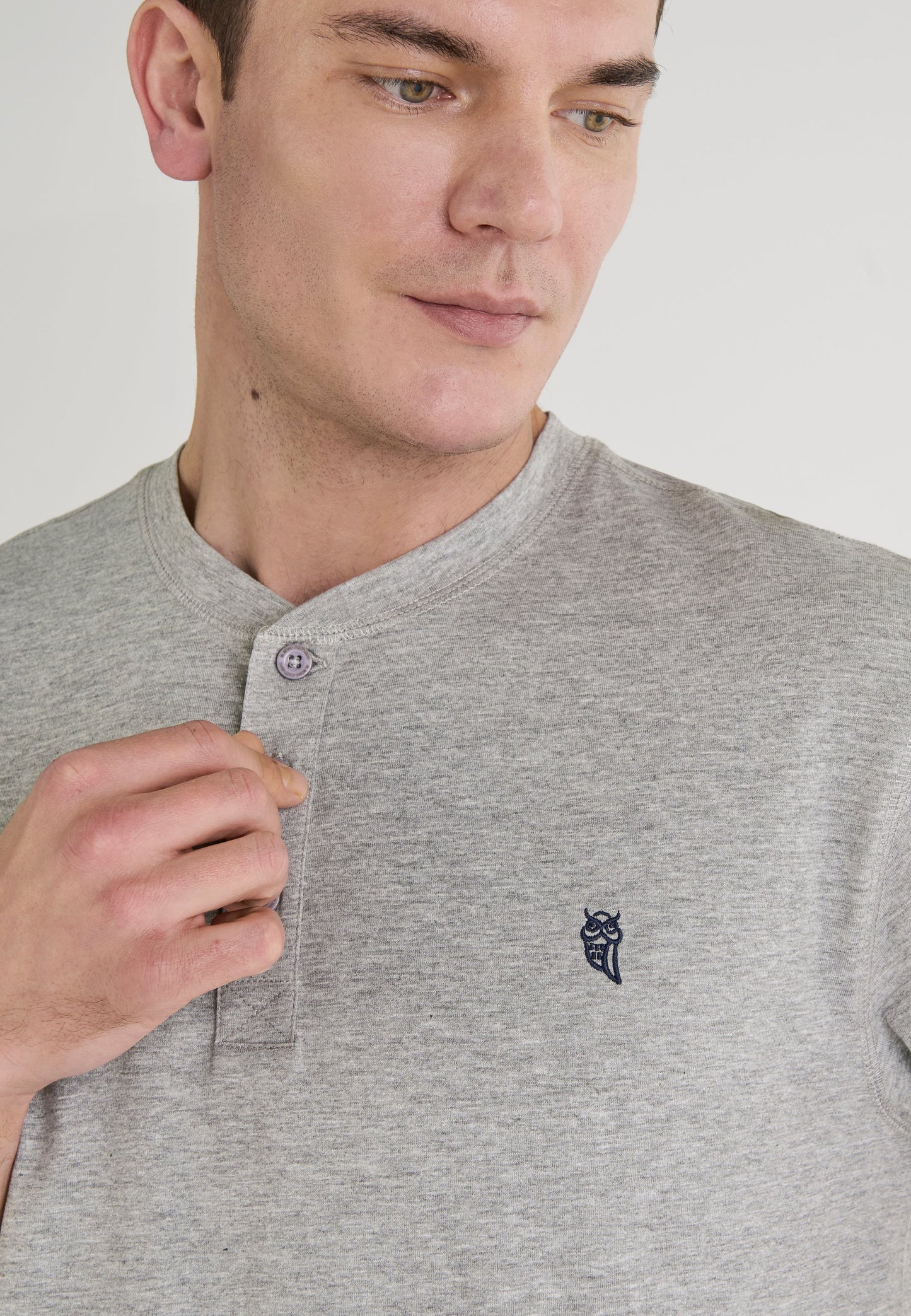 Camiseta masculina gris claro de algodón con botones y logo bordado en azul marino. Estilo casual y moderno.