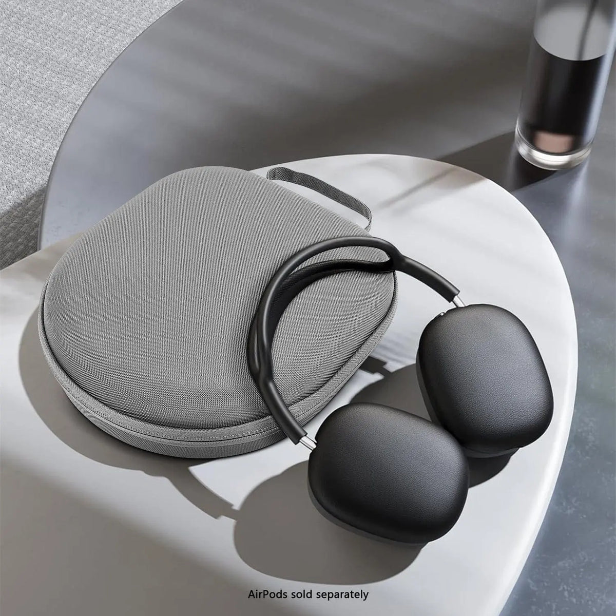 Grey fabric hardshell travel case for AirPods Max, featuring a rounded, minimalist design on a white pedestal table.