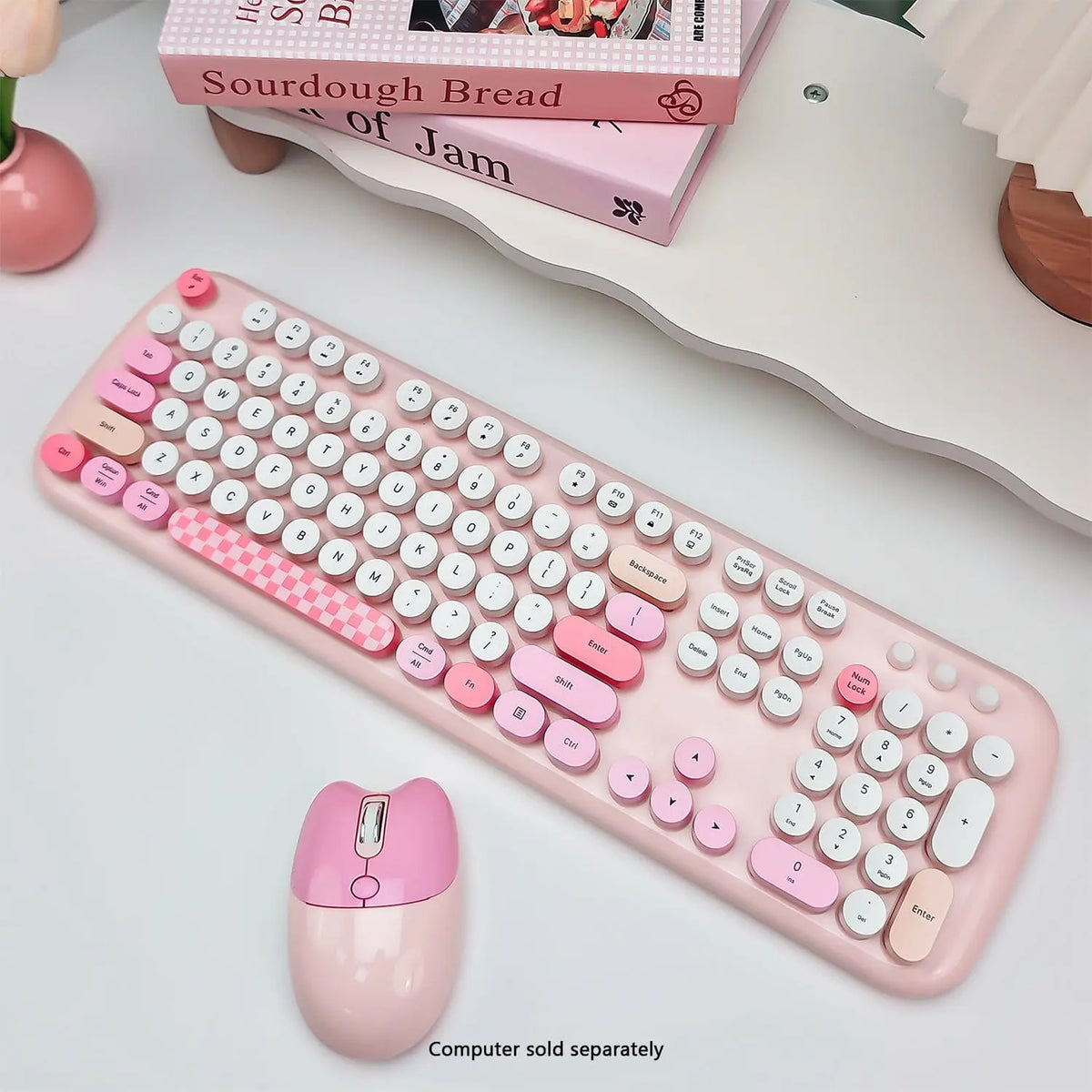 Pink wireless keyboard with round typewriter-style keys and matching mouse on a white desk with decorative books.