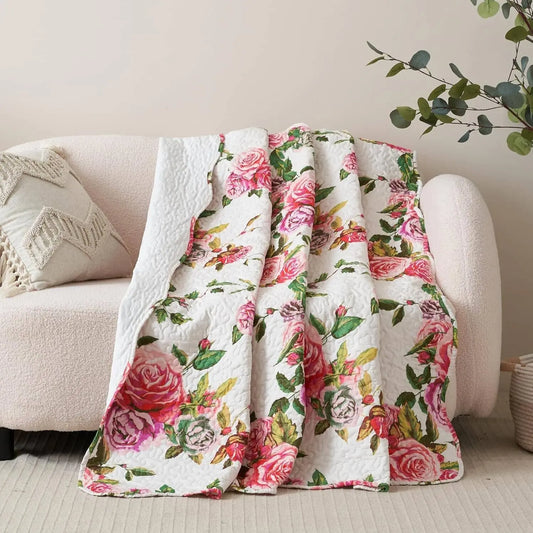 Quilted white throw blanket featuring a vibrant pink rose floral pattern, draped over a light-colored sofa.