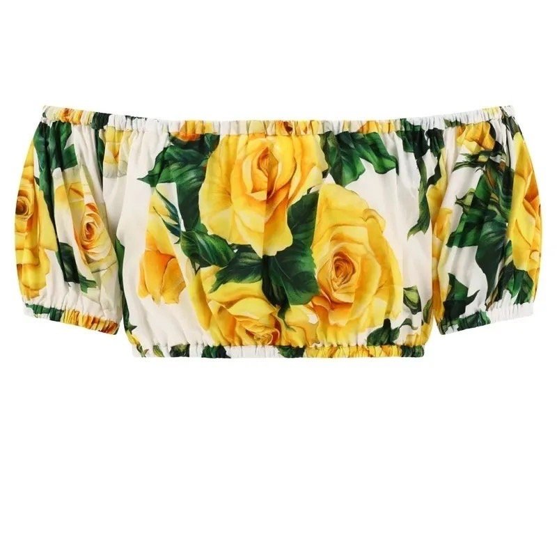 Off-shoulder white top with vibrant yellow rose print, elasticized sleeves, perfect for summer outfits.
