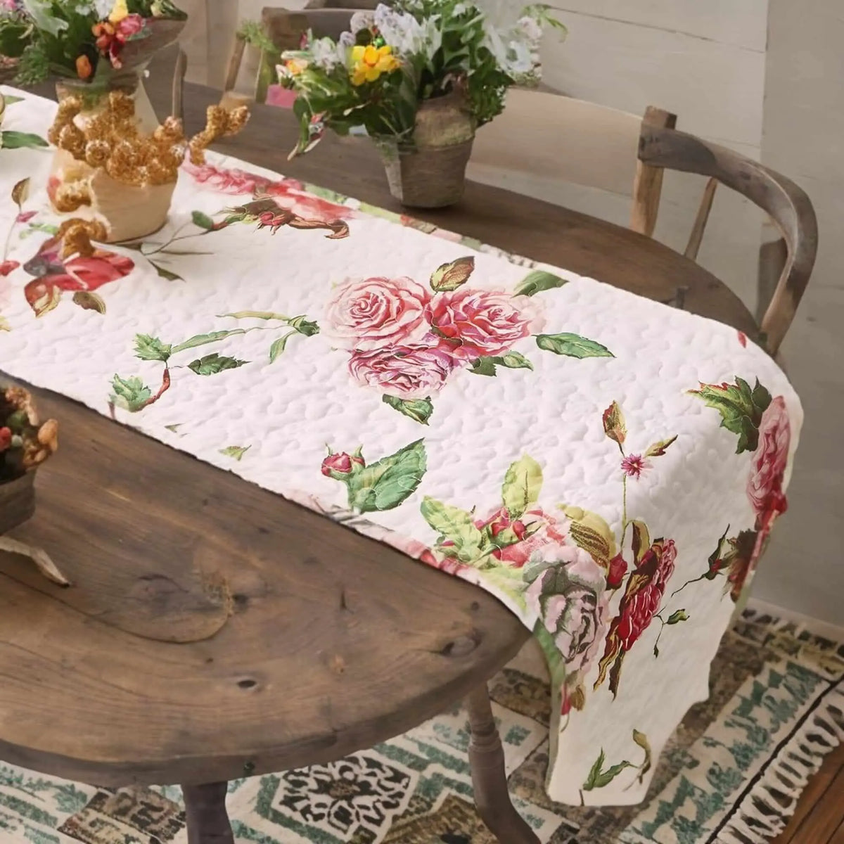 Quilted off-white table runner featuring a romantic pink rose floral pattern on a rustic wooden dining table.