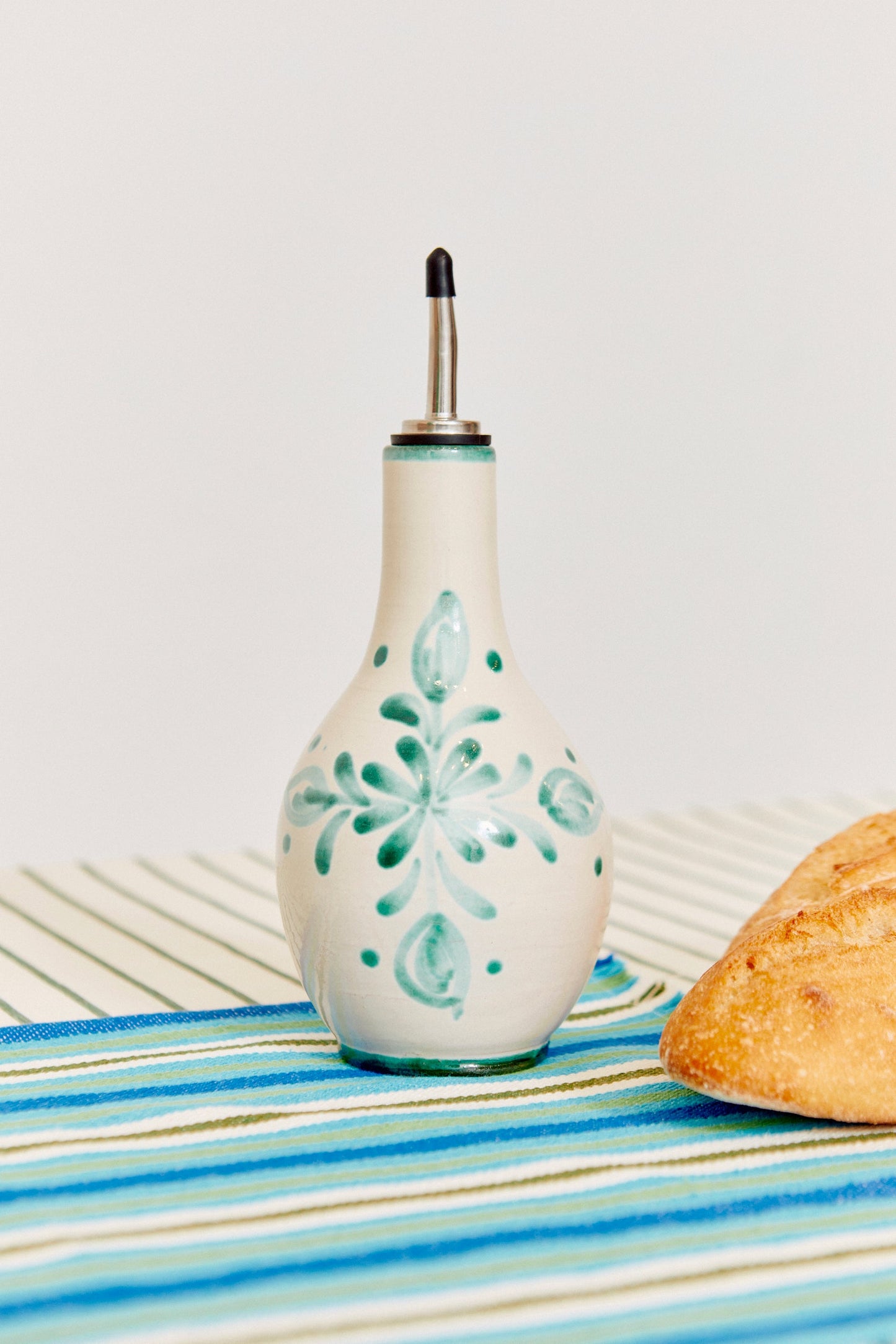 Aceitera de cerámica blanca con decoración azul, estilo rústico, sobre mantel a rayas. Ideal para cocina.