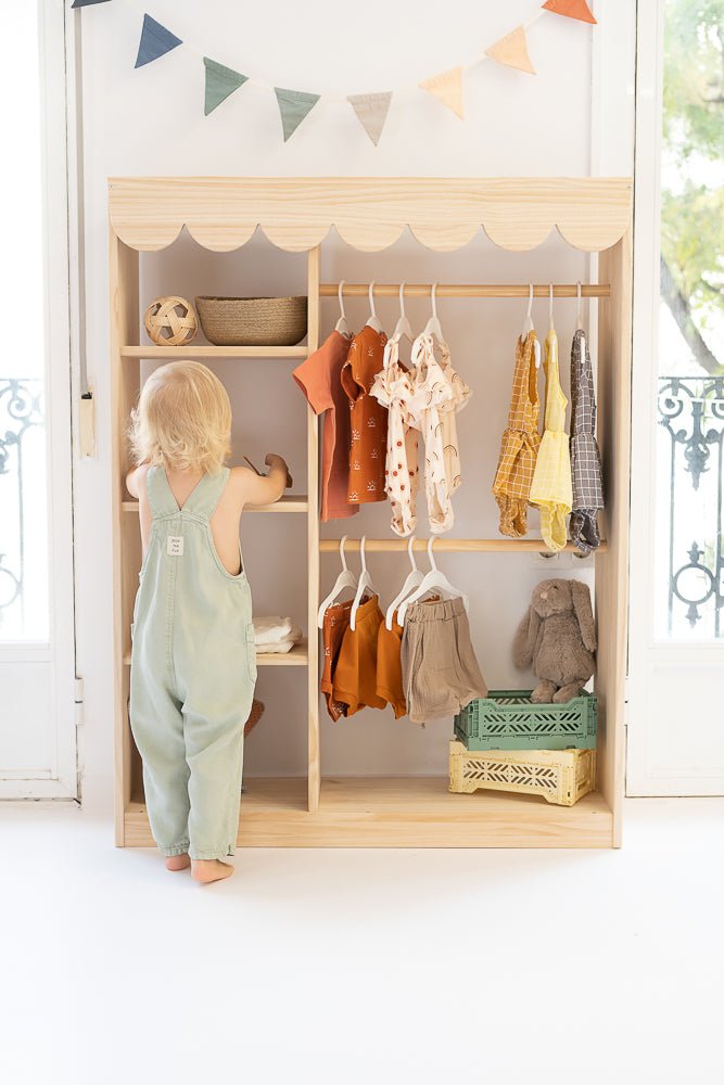 Estante de madera con ropa infantil colorida: naranjas, amarillos y tonos neutros; estilo moderno y acogedor.