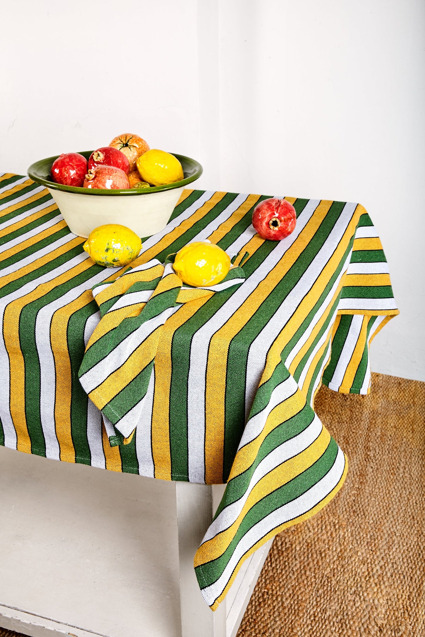 Mantel de lino a rayas verdes, amarillas y grises, sobre una mesa con frutas coloridas. Ideal para comidas informales.