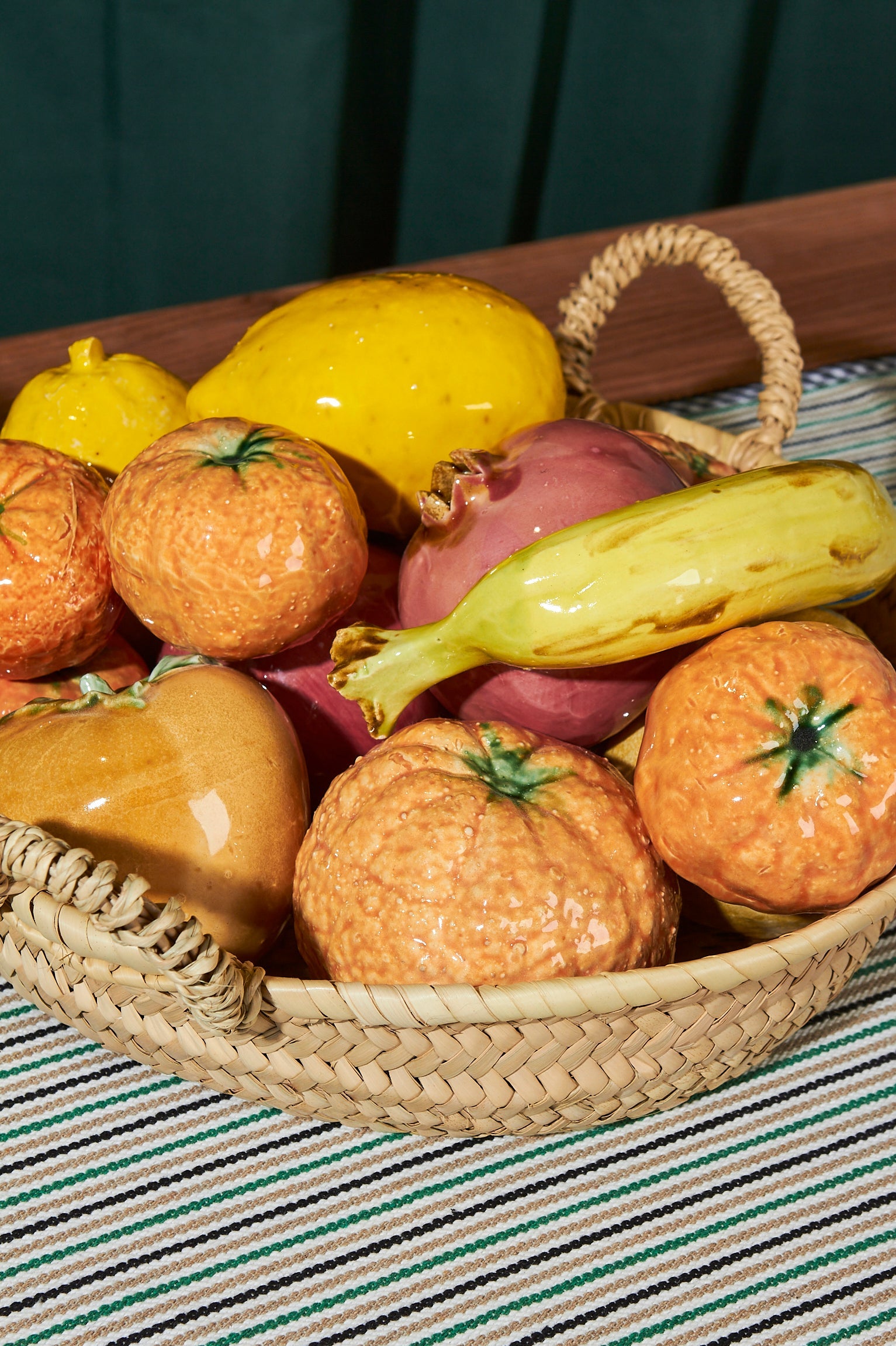 Jarrón decorativo con frutas de cerámica en tonos naranjas, amarillos y verdes, presentado en una cesta de mimbre.