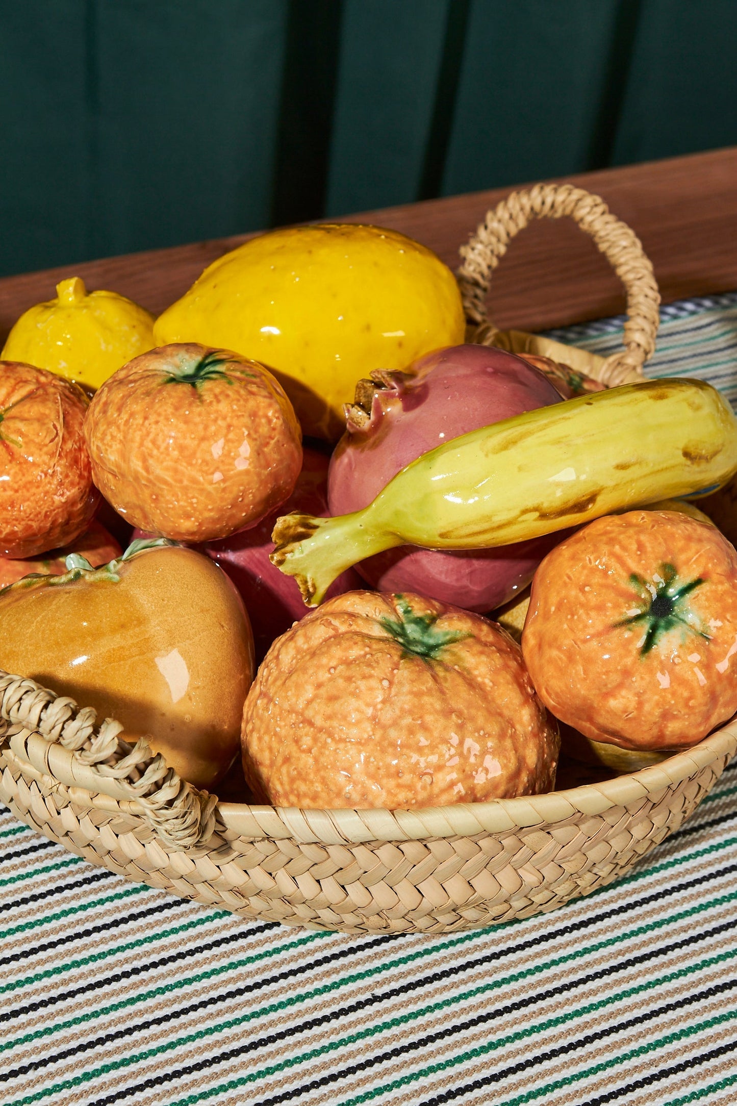 Cesta de mimbre con frutas decorativas de cerámica en tonos naranjas, amarillos y morados. Estilo rústico y moderno.