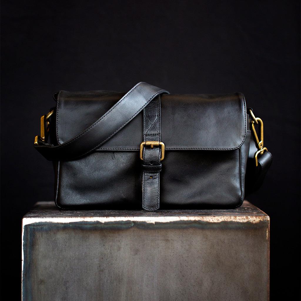 Paris black leather camera bag front view with brass buckle and side pockets