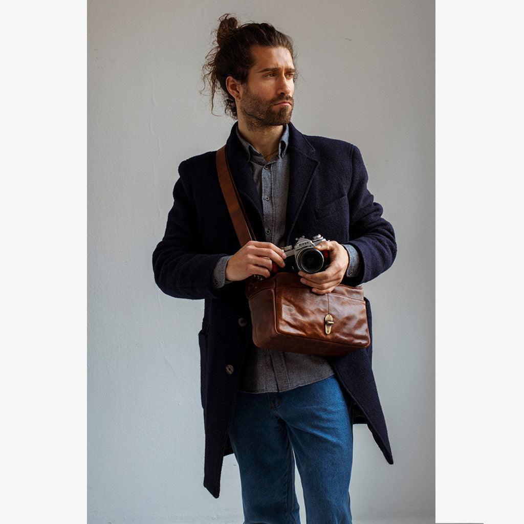 Man wearing a handmade leather camera bag París Cognac while holding a camera, showcasing elegance and craftsmanship.