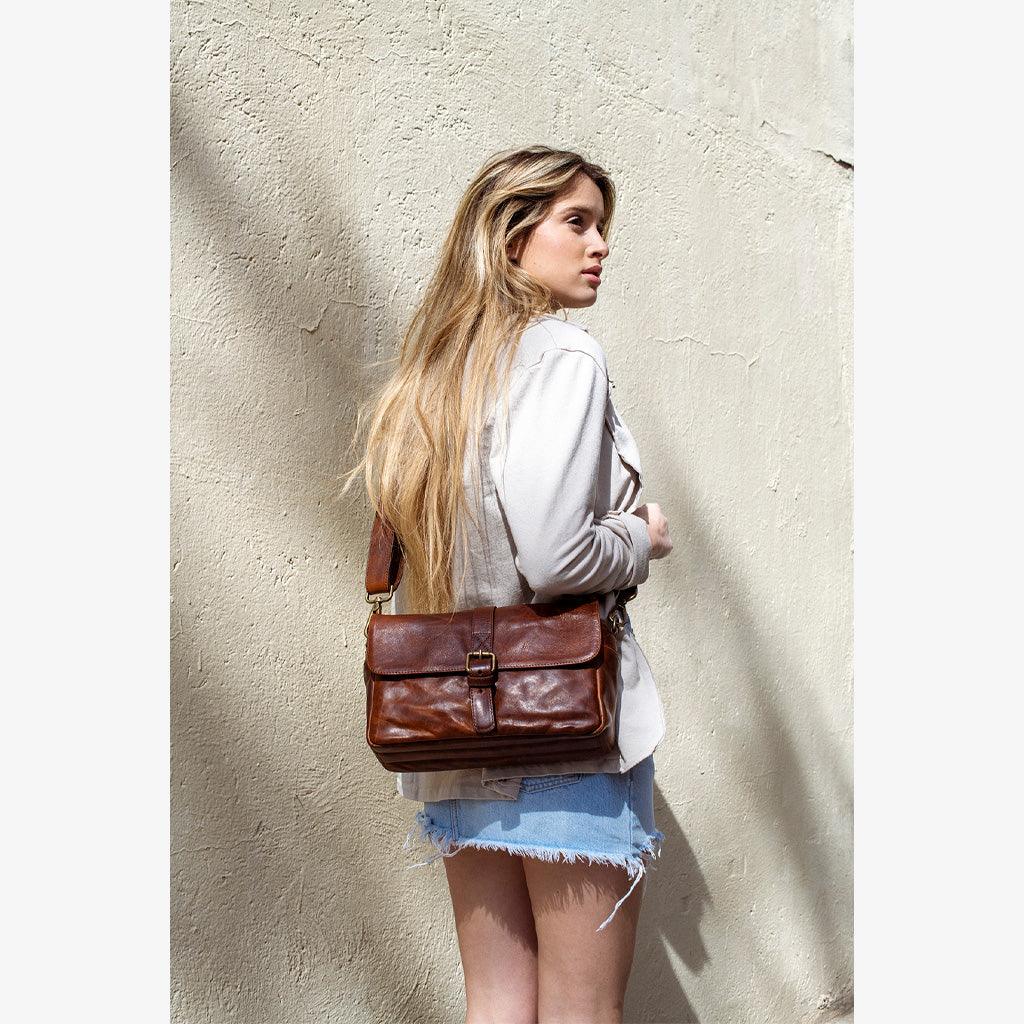 Woman wearing a Handmade leather camera bag París Cognac against a textured wall.