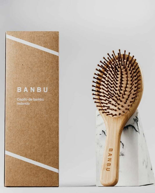 Cepillo Banbu de bambú con cerdas de madera, junto a su caja de cartón reciclado sobre una base de mármol.