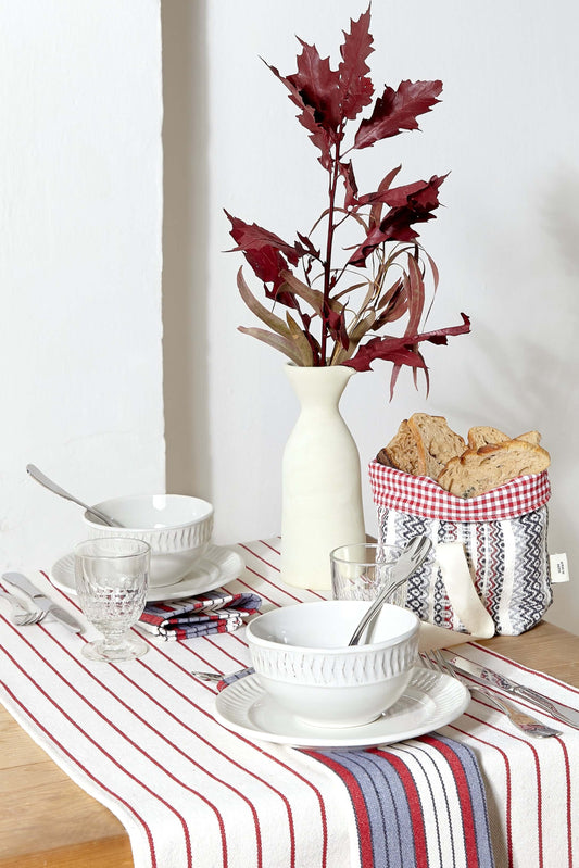 Camino de mesa granate con rayas, vajilla blanca y centro decorativo con hojas otoñales y panera