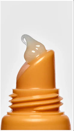 Close-up of a mango-orange lip balm tube with a dollop of translucent, glossy balm emerging from the applicator tip.